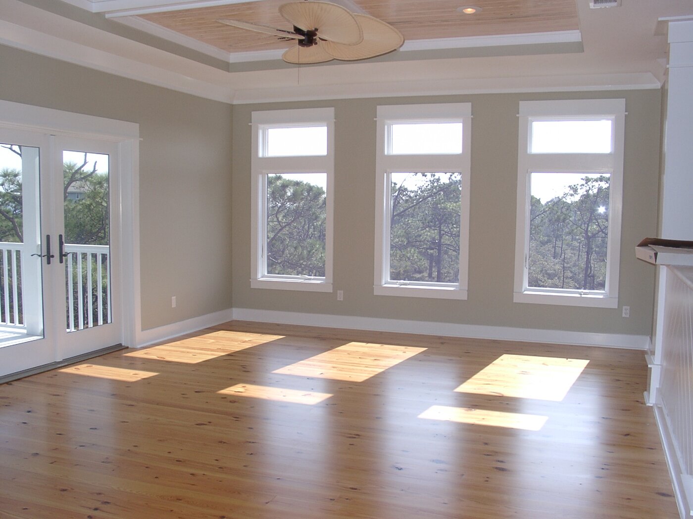 Finished hardwood flooring installation in a bright room with large windows